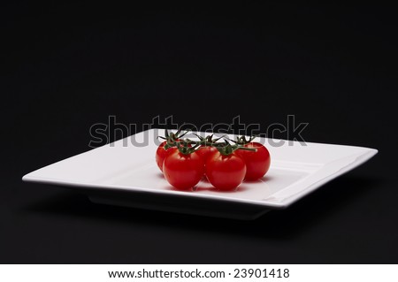 Five cherry tomatoes on a white plate with black background.