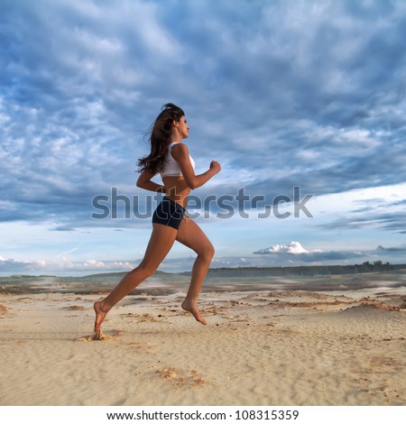 Running barefoot woman. Female runner jogging during outdoor workout on sand at evening. Beautiful  Fitness model outdoors.