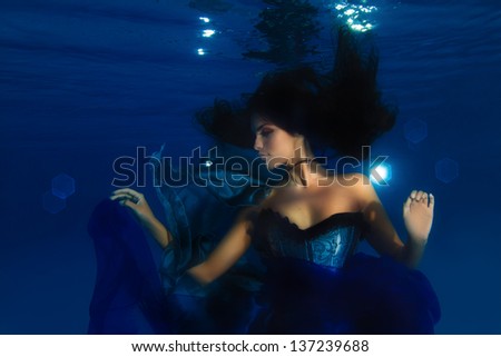 Beautiful underwater fashion model with dark long hair playing with blue fabric