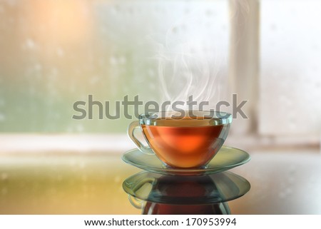 Hot steamy black tea in front of a window glass in an autumn rainy day