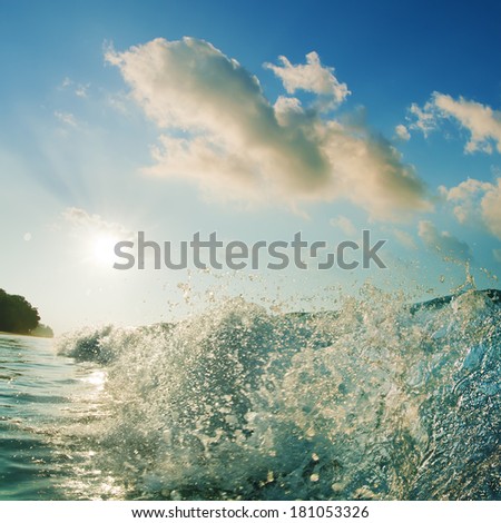 beautiful tropical beach with breaking splashing wave under bright sunlight