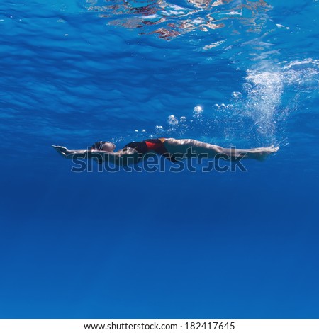 Professional female swimming on her back underwater in blue with air bubbles under water surface