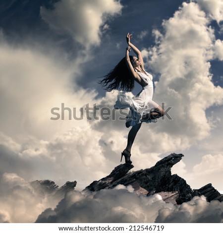 Creative cloudy background. Young girl wearing gorgeous white dress dancing with expression