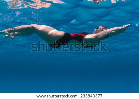 Professional female swimming underwater in blue sea with mirror on water surface and caustic effect on her skin
