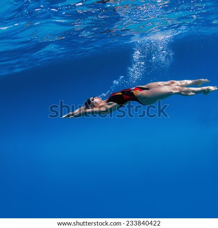 Professional female swimming underwater in blue sea with mirror on water surface and caustic effect on her skin