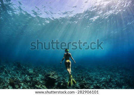Freediver Girl in yellow bikini wearing yellow fins beholding beautiful coral reef underwater. Maldivian diving with rays of Sun.