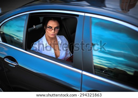 Business woman in a black car on backseat after hard day. A Brunette Lady sitting in a luxury vehicle holding folder with documents looking from open window.