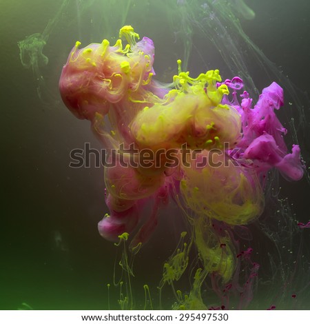 Yellow and pink complementary colors of ink in water in a shape of clouds. Colorful ink and paint swirling underwater on dark background.