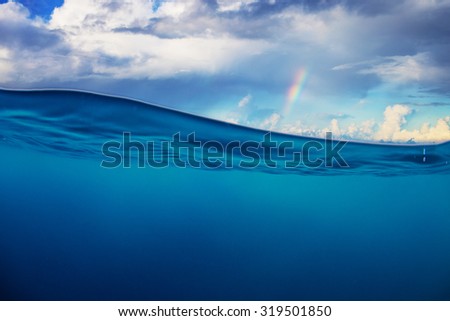Abstract marine design template. Cloudy sky with rainbow splitted by waterline. Blue deep ocean.