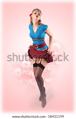 Pinup style 60x blonde girl in blue blouse with turquoise and plaid skirt and red flower in her hair on pink background