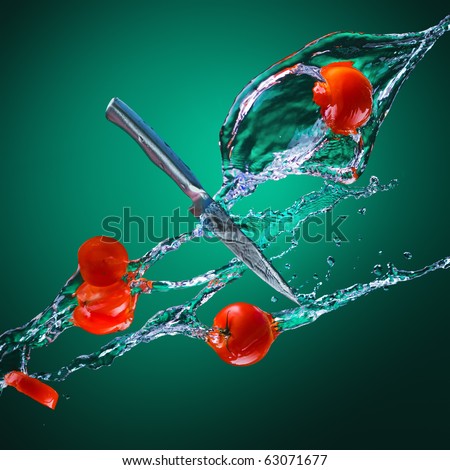 a steel knife and a few whole juicy bright red tomatoes and cut in the jets of water on a green background