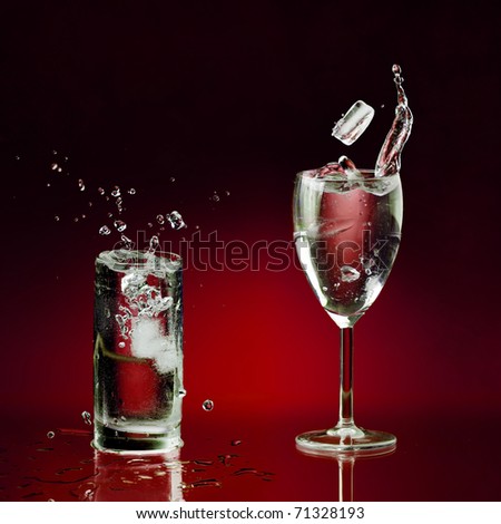 two clear glasses of water standing on wet surface and few pieces of ice dropped with splashes and bubbles