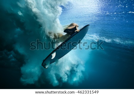 Beautiful Surfer Diving Duckdive under Big Ocean Wave. Turbulent air bubbles and tracks after sea wave crashing. Ripples at water surface with sky color.