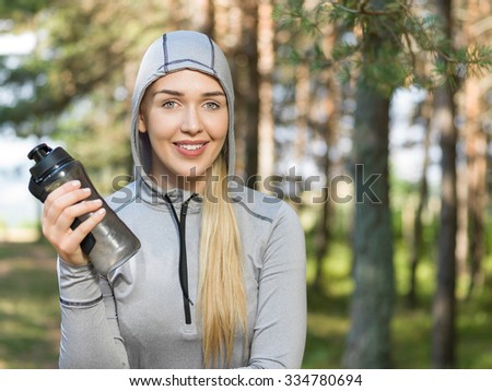 Beautiful woman drinking water on a sunny day in nature after jo