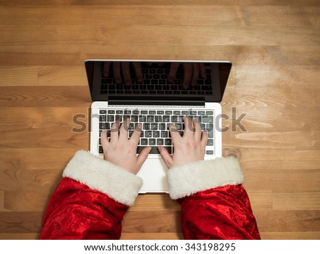 Santa working at desk and typing on a laptop, Christmas gifts and letters, hands top view