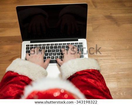 Santa working at desk and typing on a laptop, Christmas gifts and letters, hands top view