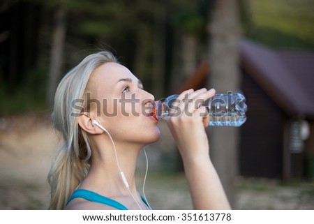 Beautiful woman drinking water on a sunny day in nature after jo