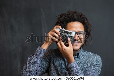 Portrait of a smiling afro american man making photo on retro camera on chalkboard