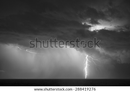 Black and white of a lightning bold striking the surface of the ocean during a thunder storm.