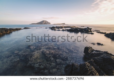 Calm waters of a tide pool off the east coast of Oahu, Hawaii during sunrise with two islands on the horizon