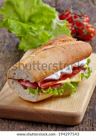 Sandwich with serrano ham and vegetables on wooden cutting board
