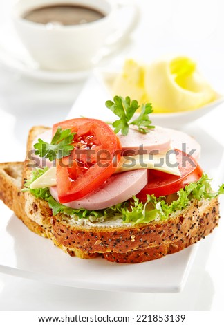 breakfast sandwich with sliced sausage and tomato on white plate