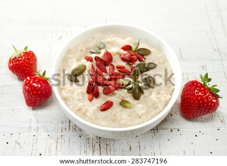 oat porridge with healthy goji and squash seeds on white wooden table