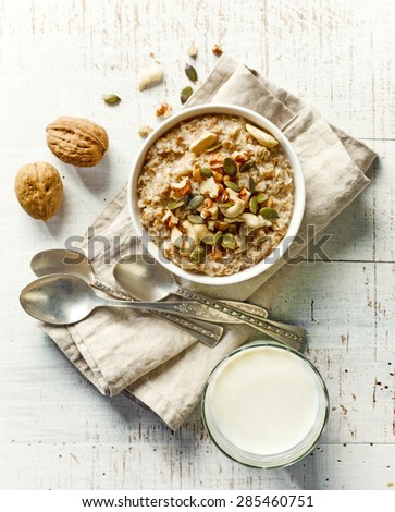 bowl of breakfast porridge with nuts and milk on white wooden table, top view