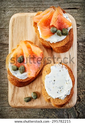 toasted bread slices with cream cheese and smoked salmon on wooden cutting board, top view