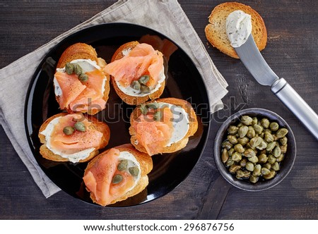 toasted bread slices with smoked salmon fillet and cream cheese on black plate, top view
