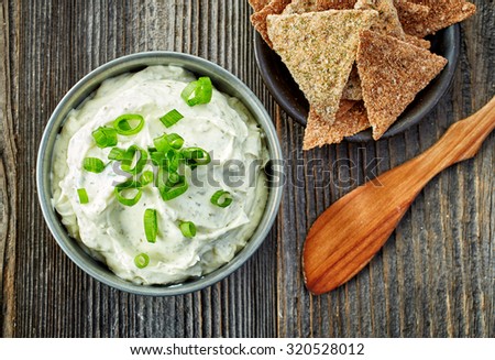bowl of cream cheese with green onions and herbs, dip sauce on wooden table, top view