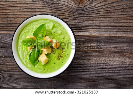 bowl of broccoli and green peas cream soup on wooden table, top view
