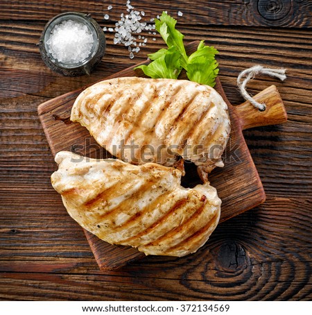 grilled chicken fillets on wooden cutting board, top view