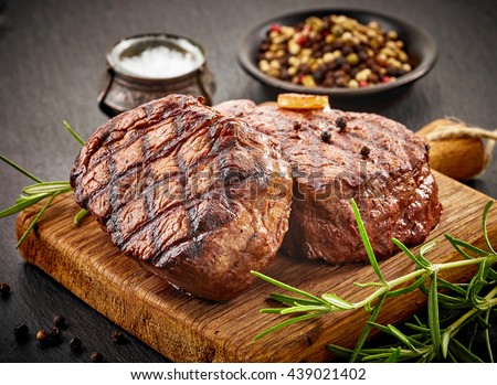 grilled beef steaks with spices on wooden cutting board