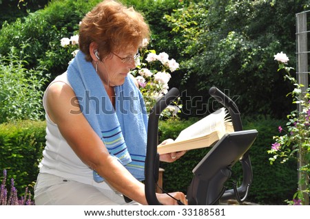 Senior woman working out on the fitness bike while reading a book