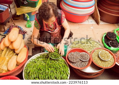 Seoul, South Korea - August 28, 2014: A Korean woman crouches down to sort through a bin of fresh peppers at the Gwangjang Market.