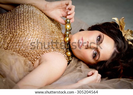 Golden Model lying on ground holding her necklace