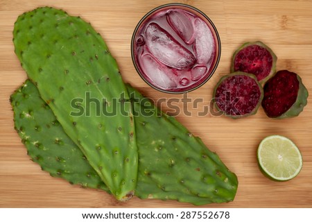 A Prickly Pear (a.k.a. cactus fruit) Margarita, surrounded by cactus leaves, prickly pears, and lime.