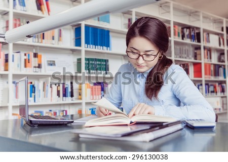 young woman student studying and looking in book and writing down in the library