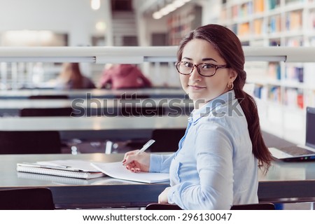 young woman student studying and looking in book and writing down in the library