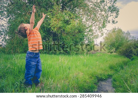 Child near a stream with his arms up in the air.