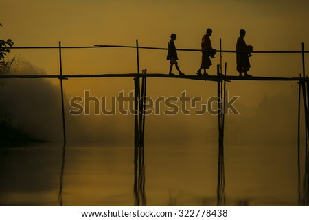 Novice less alms round on a wooden bamboo bridge  at sunrise Silhouette thailand
monks receive food offering  Thailand. Offering food is one of most common rituals in Buddhism.