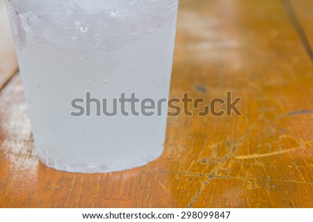 A bottom cup that have ice-water on left of orange-brown wood background