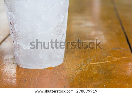 A bottom cup that have ice on left of orange-brown wood background
