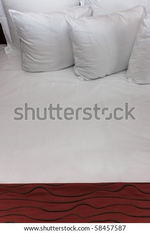 Fluffy white pillows against a white sheet with a red blanket.
