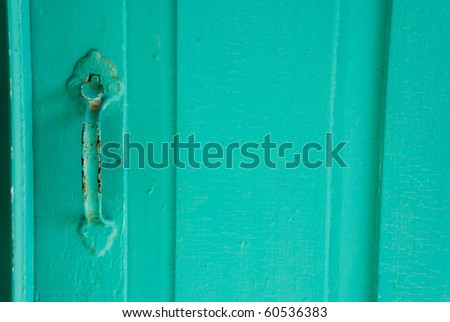 Classic antique metal door handle painted teal, now chipped and rusted on wooden door.