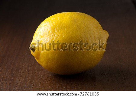 A single fresh yellow lemon on a wood grain table against a black background.