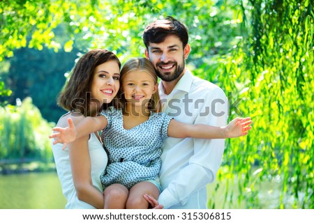 Stretching hands of happy daughter with parents. Rest time of family. Outdoor family picnic under green trees.