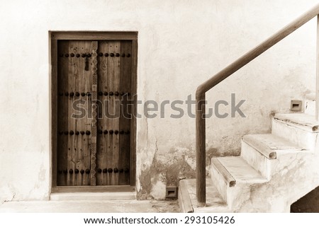 A stairway leads to the roof from a carved wooden door of the restored Shaikh Salman house in Muharraq, Bahrain. The door is typical of traditional Arabian Gulf architecture.