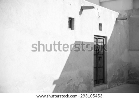 Black and white picture of a traditionally carved wooden door in the corner of the courtyard of the restored Shaikh Salman house, Bahrain with drains to carry rainwater away from the adobe walls.